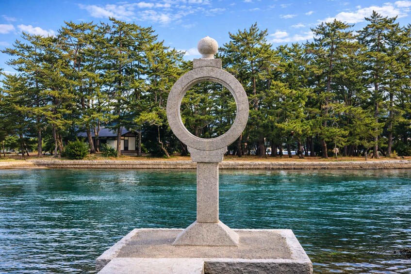 Un monumento in pietra con sommità circolare e ornamento sferico, immerso in uno specchio d'acqua sullo sfondo di alberi e cielo sereno. 4