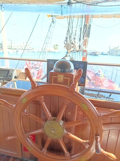 Una rueda de timón de madera, cuerdas y vista de un puerto deportivo con barcos. 5