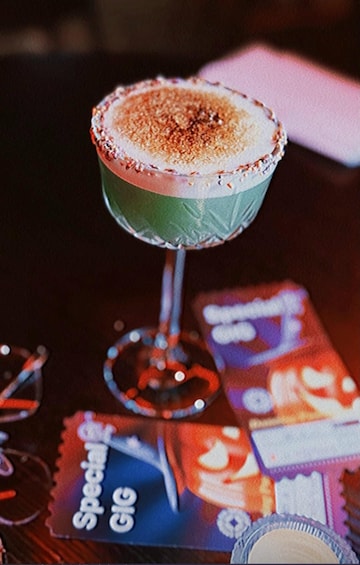 En cocktail i et glas med saltet kant, en flaske Special Gig, og en æske af samme mærke på et bord. 3