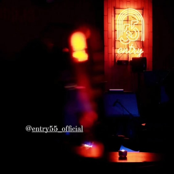A dimly lit room with a neon sign that reads 'entry55' and a microphone stand. 4