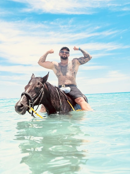 En mand med tatoveringer rider på en hest i lavt vand. 1