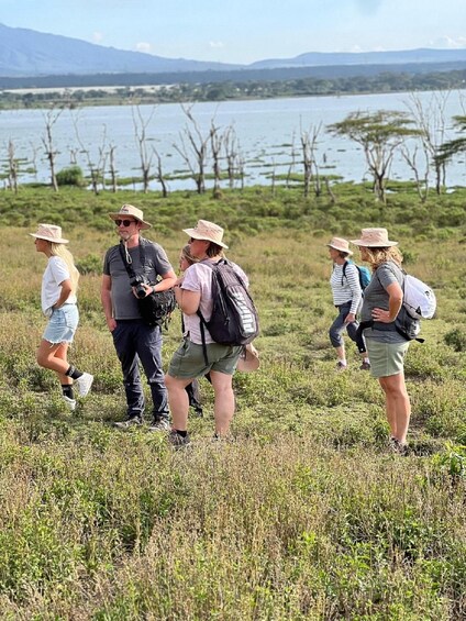Un gruppo di persone fa un'escursione in un prato erboso, con un lago e montagne sullo sfondo. 4