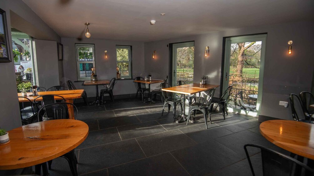 An indoor dining area with wooden tables and chairs, large windows, and pendant lighting. 3