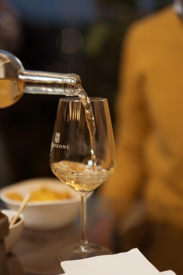 Et gennemsigtigt vinglas med etiket, der fyldes med en klar væske, sandsynligvis vin, fra en flaske. 3
