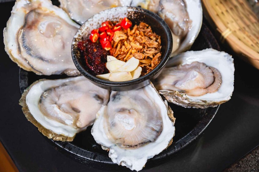 A plate of oysters with a dipping sauce and garnishes. 4