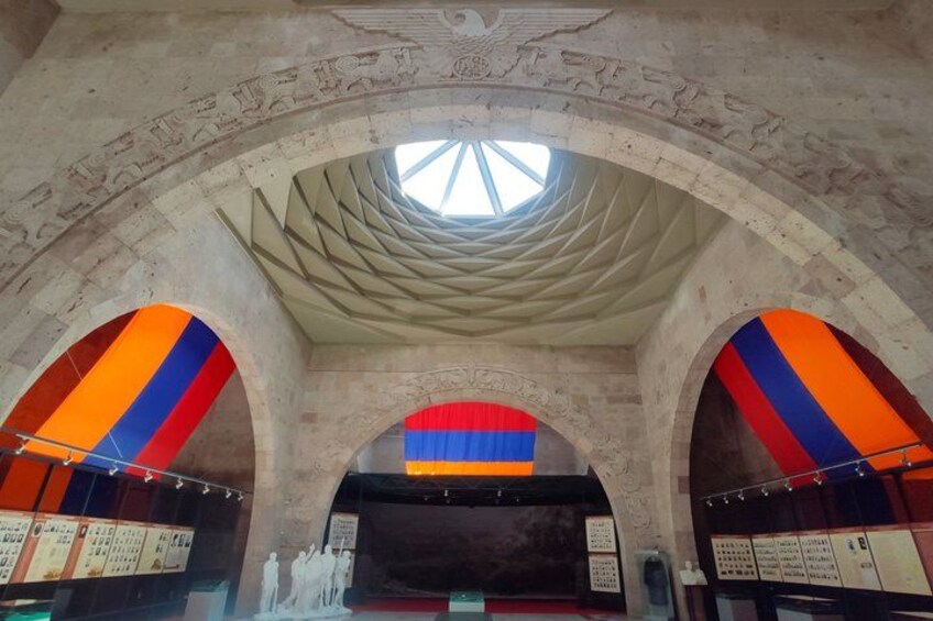 An interior with arched ceilings, a central skylight, and colorful stained glass windows. 1