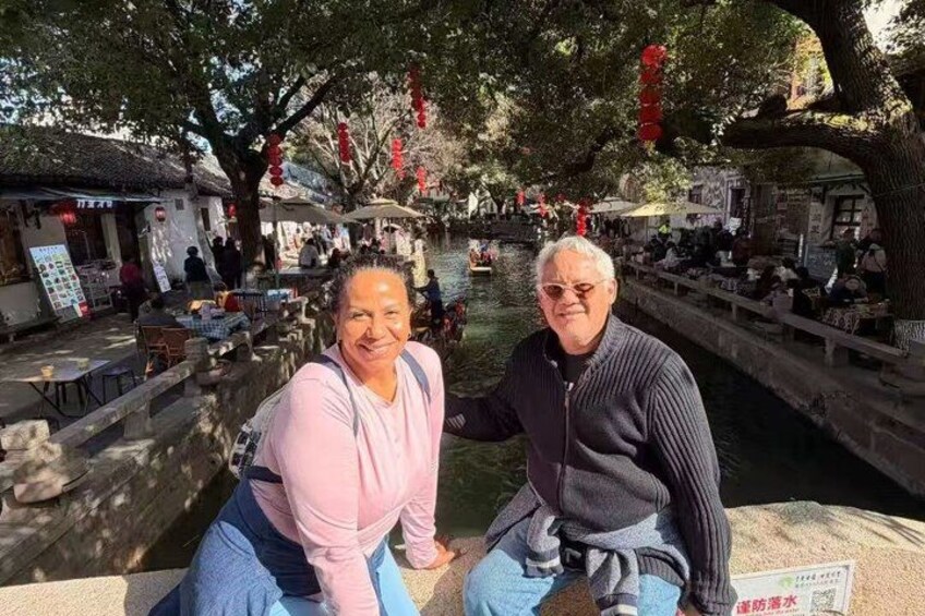 A couple sitting by a canal with traditional buildings and red decorations in the background. 4