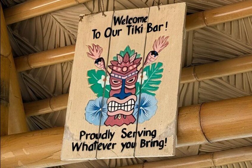 A sign with a tiki bar welcome message and a cartoon tiki character. 3