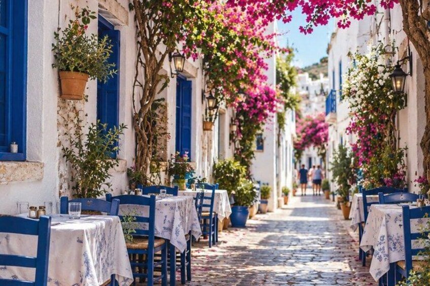 A narrow street with white buildings, blue shutters, and tables set up for outdoor dining. 5
