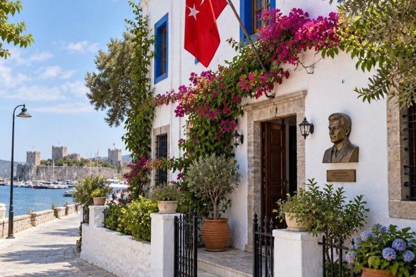 A white building with a red flag, a bust, and bougainvillea vines. 2
