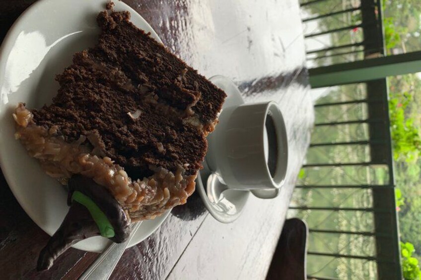 A slice of chocolate cake on a white plate, a white mug, and a wooden table. 2