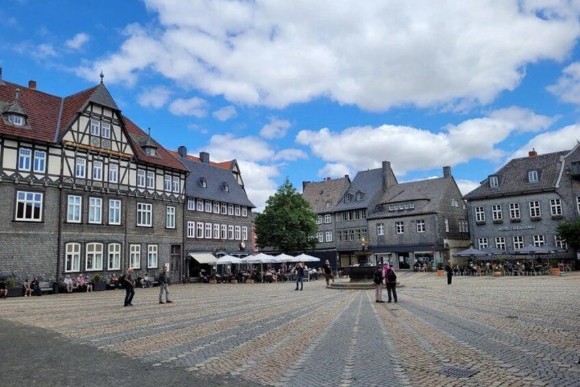 A cobblestone square with historic buildings, a tree, and people walking. 3