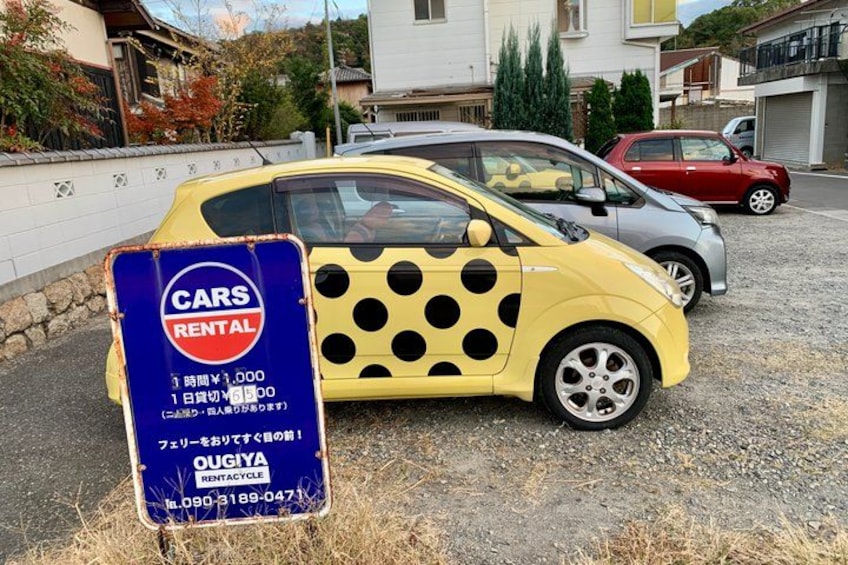 A yellow car with black spots parked in front of a rental sign. 2