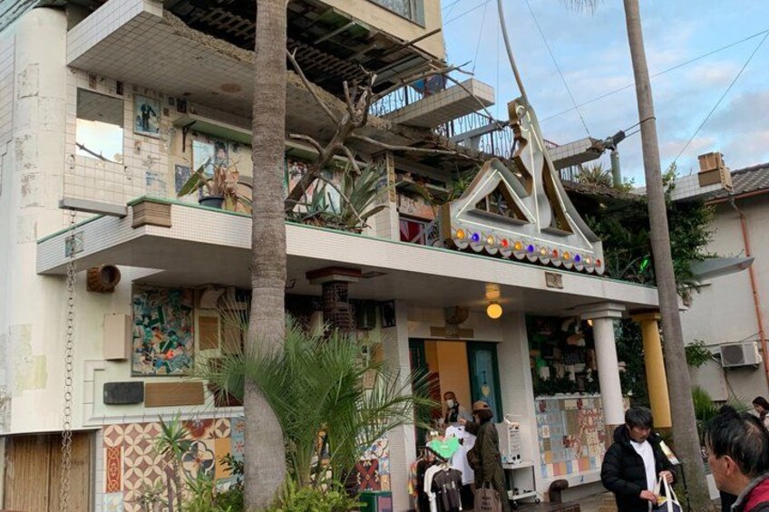 A multi-story building with a colorful facade, a balcony with plants, and a person standing in front. 5