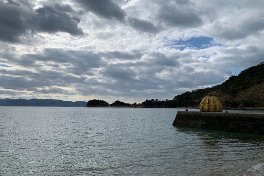 A body of water with a large yellow spherical structure on a dock, a cloudy sky, and distant landforms. 4