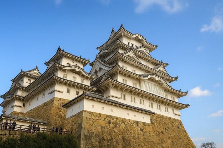 A large, multi-tiered castle with traditional architecture, a stone base, and a clear sky. 1