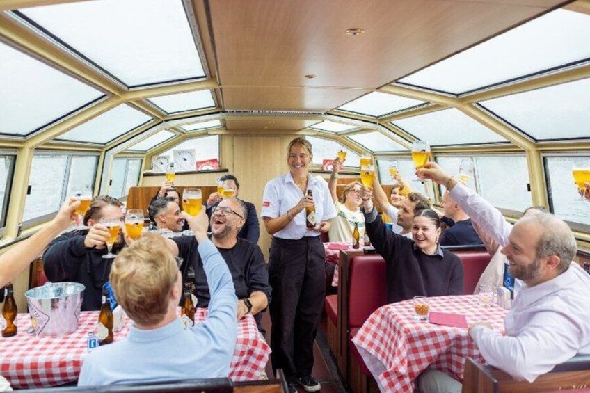 A group of people toasting with drinks on a boat with red and white checkered tablecloths. 2