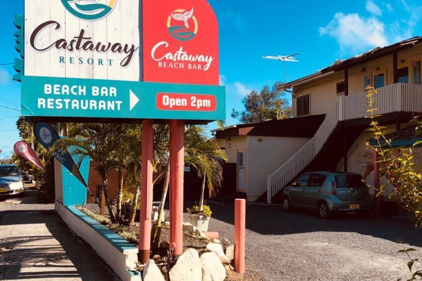 A beach bar and restaurant sign for Castaway Resort, with a clear sky and a building in the background. 3