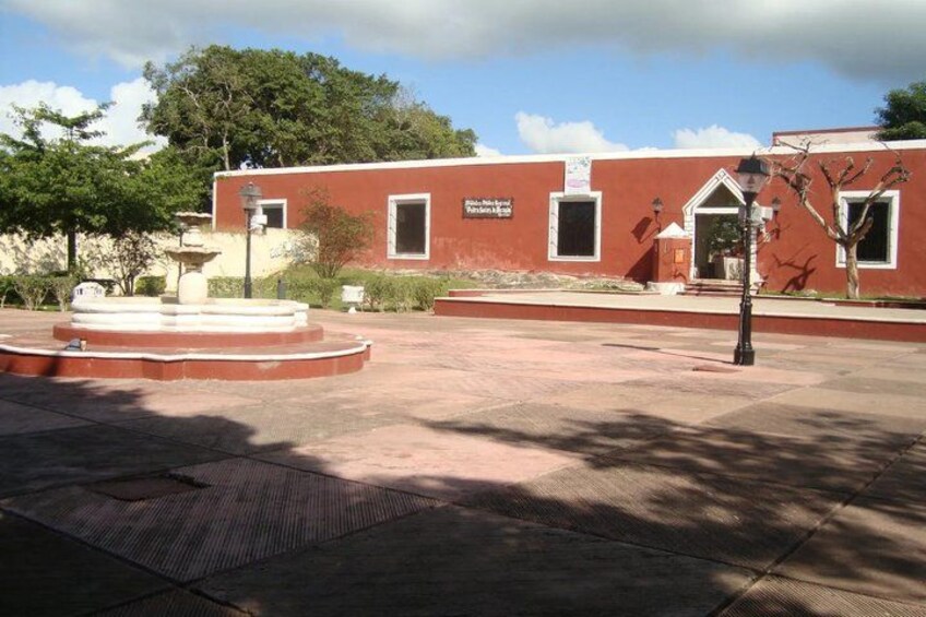 A red building with a sign, a fountain, and a tree in a courtyard. 3