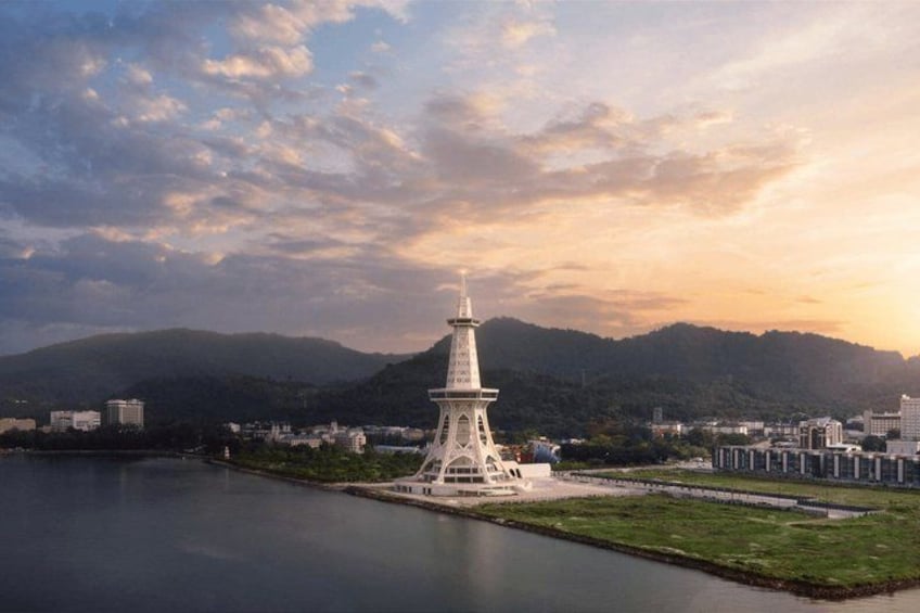 A tower by a body of water with a mountainous backdrop. 1