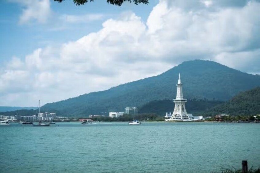 A coastal cityscape with a prominent white tower, a mountain in the background, and several boats on the water. 4