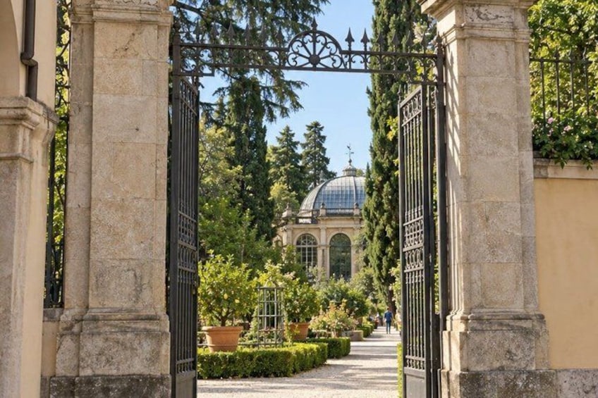 A garden pathway leading to a building with a dome, flanked by stone columns and a wrought iron gate. 3
