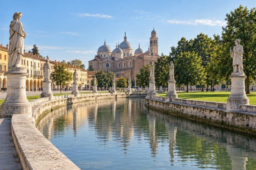 A canal with statues, a large building with domes, and trees. 4
