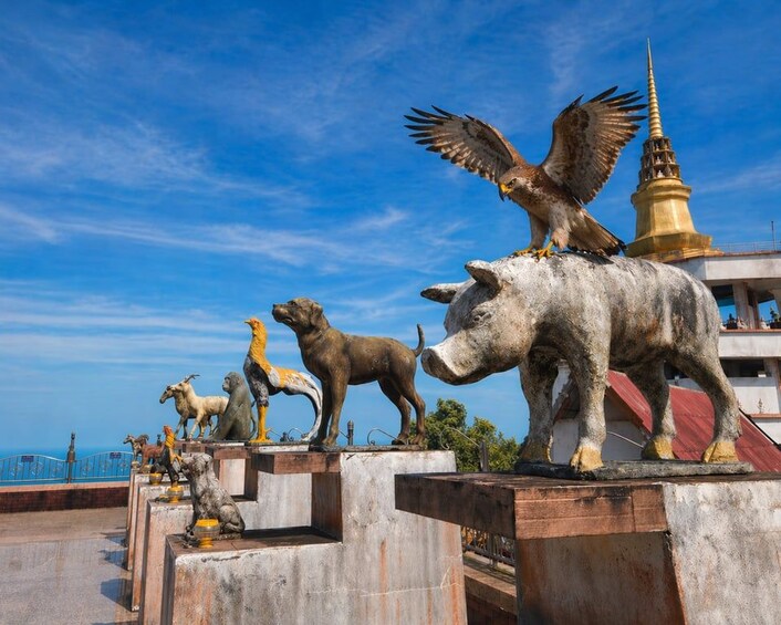 A series of animal statues, including a bull, a lion, and a bird of prey, on a concrete platform with a golden spire in the background. 2