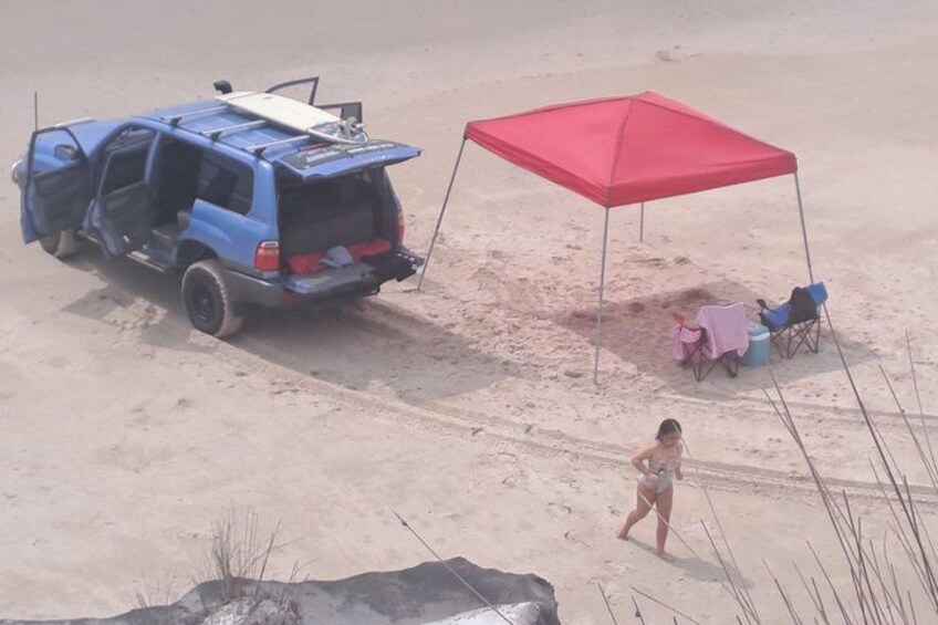 A blue SUV parked on a sandy beach with a red canopy and beach chairs. 3