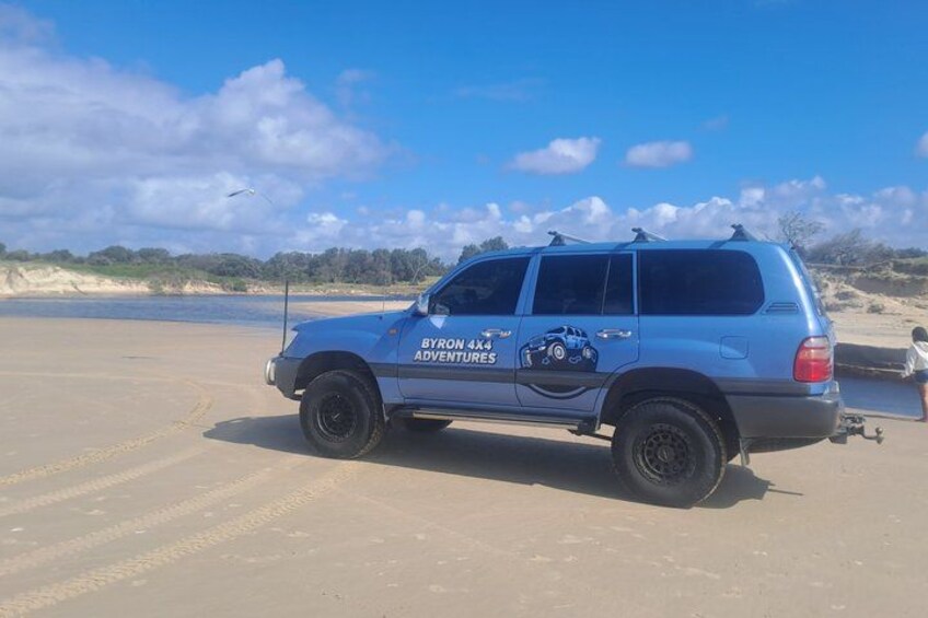A blue 4x4 vehicle with 'Byron 4x4 Adventures' on the side parked on a sandy beach. 2