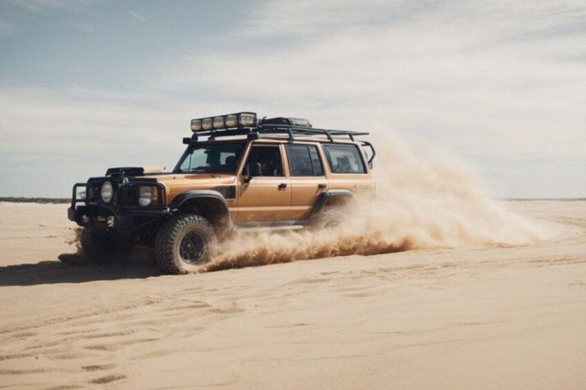 A beige off-road vehicle driving through a desert with sand being kicked up by its tires. 5