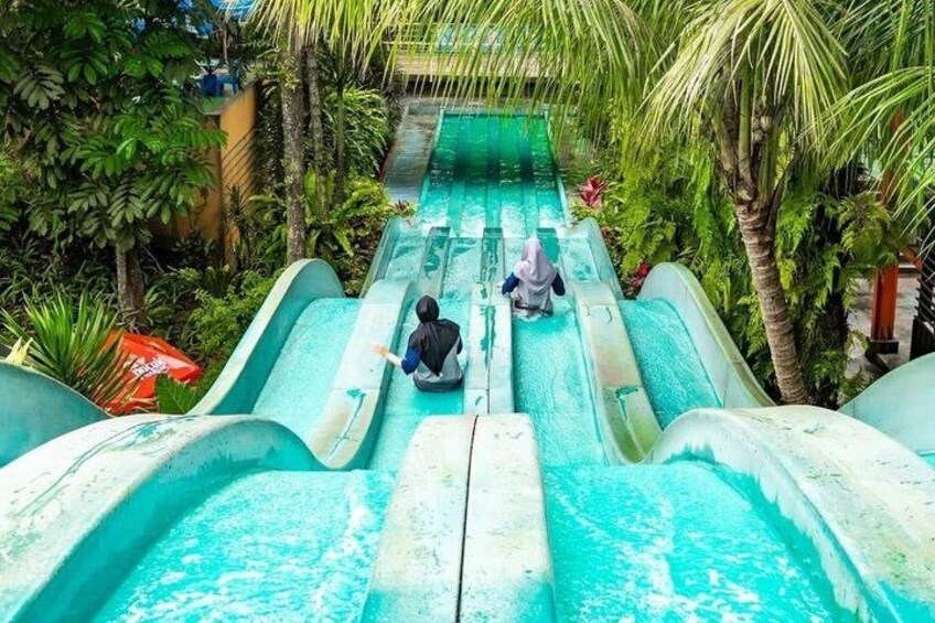A water slide with two people sliding down, surrounded by lush greenery. 5