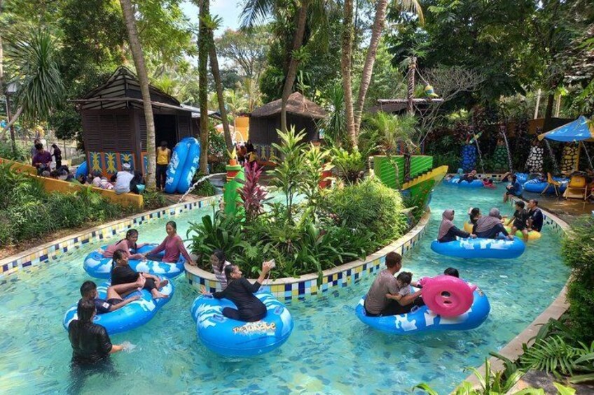 People floating in water on inflatable rings in a tropical setting with palm trees and a pool. 3
