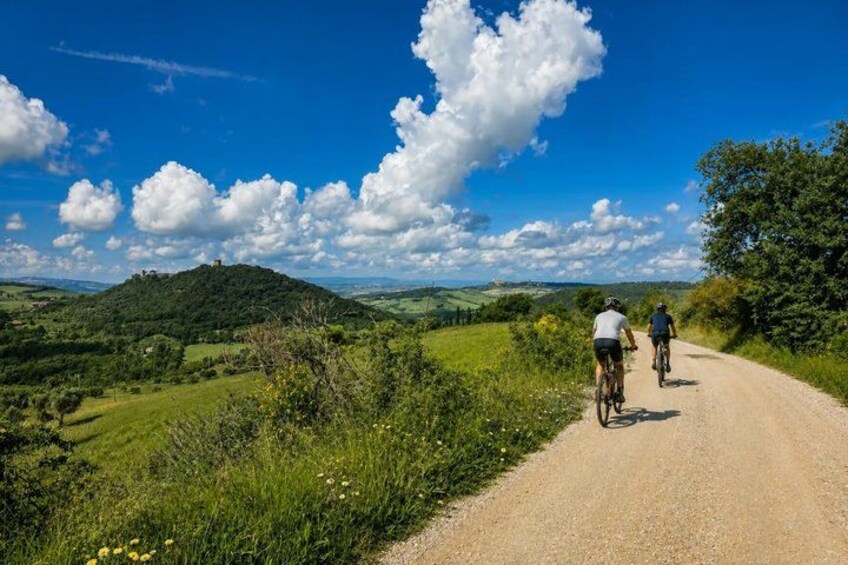 A dirt road with cyclists, green hills, and a clear blue sky. 4