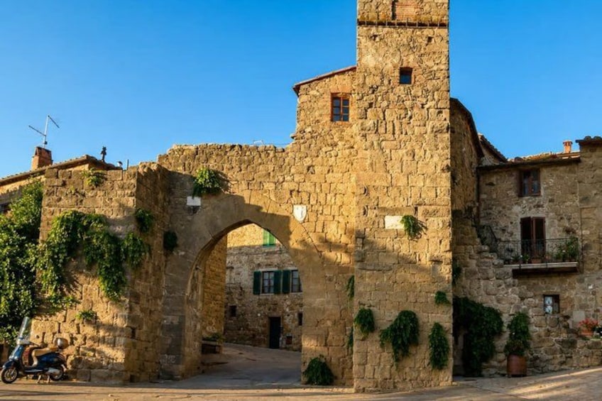 A stone archway with a tower, surrounded by buildings and greenery. 2