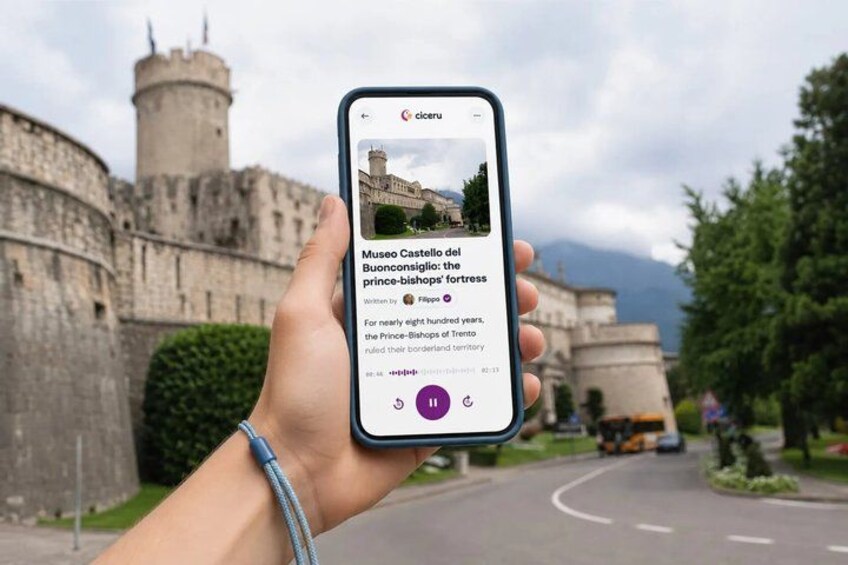 A hand holding a smartphone displaying a photo of a historic castle with a moat and a tower. 1