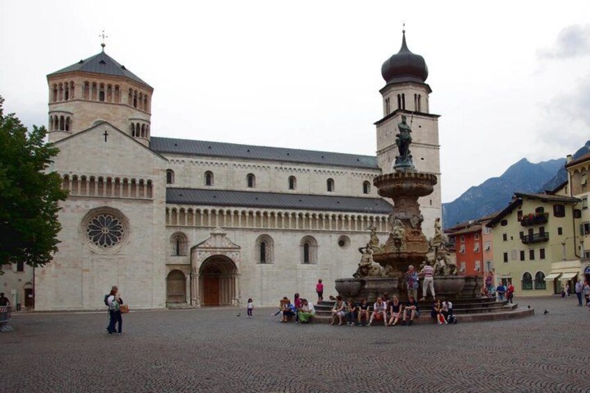 A historic building with a fountain, cobblestone plaza, and mountains in the background. 3