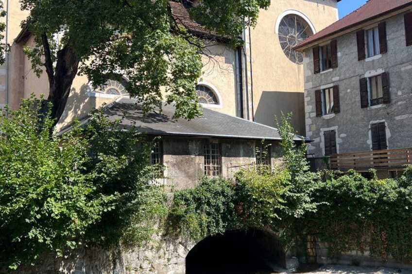 A stone bridge with a tunnel entrance, surrounded by lush greenery and historic buildings. 5
