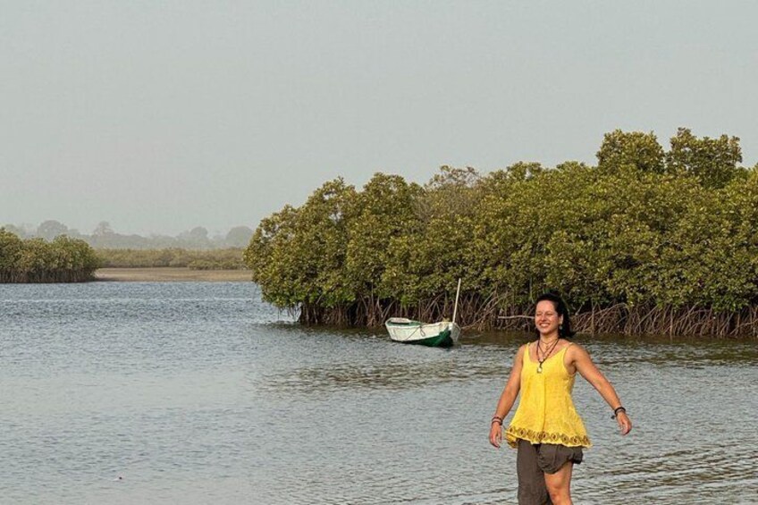 A person standing in water with a boat and mangrove trees in the background. 2
