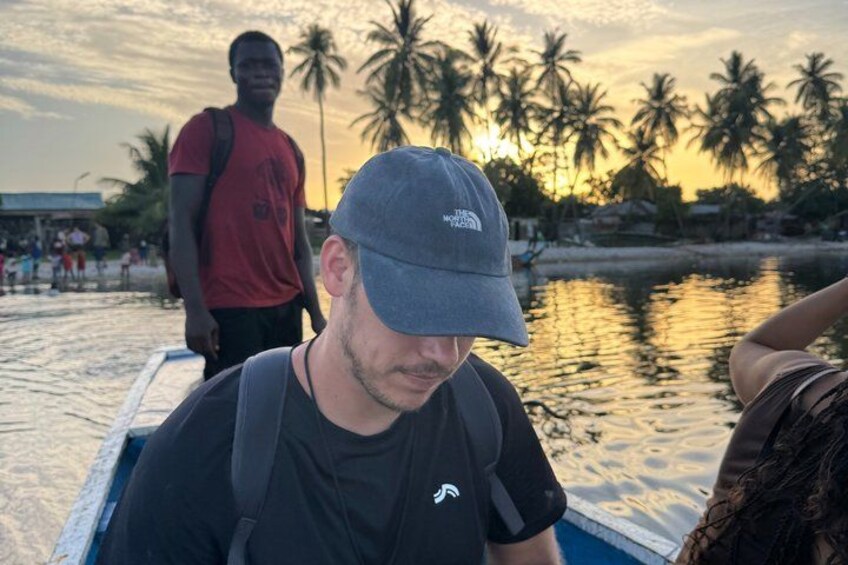 A person wearing a grey cap and black shirt, a boat, palm trees, and a sunset. 5