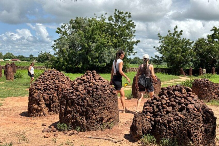Two people walking near large mounds of earth, with trees and a cloudy sky in the background. 3