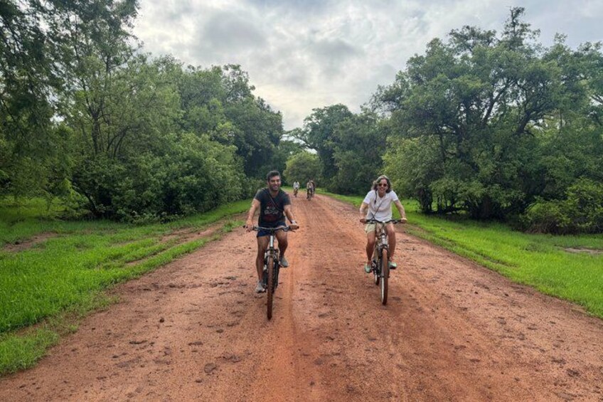 Two people riding bicycles on a dirt road surrounded by greenery. 5