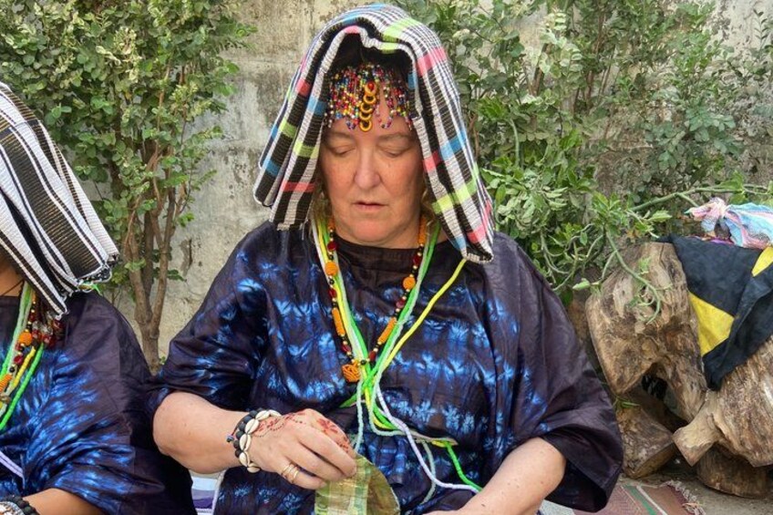 A person wearing a blue patterned shirt and a striped headscarf, holding a green object. 2