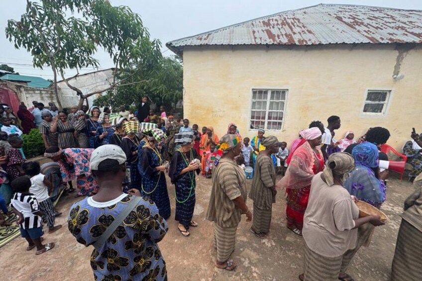 A group of people gathered outdoors in front of a building with a corrugated metal roof. 5