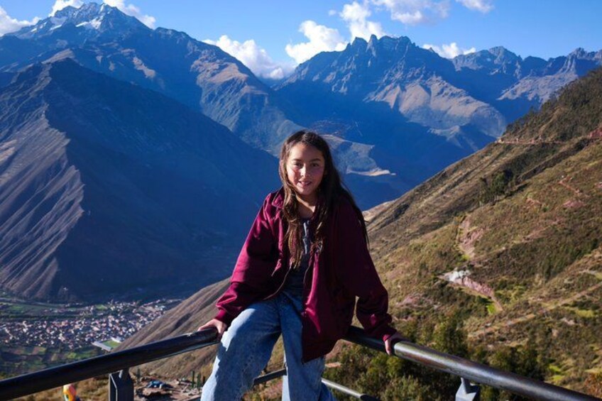 A person sitting on a railing overlooking a mountainous landscape with a valley below. 3
