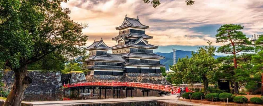 A traditional Japanese castle with multiple tiers, surrounded by lush greenery and a red bridge. 4