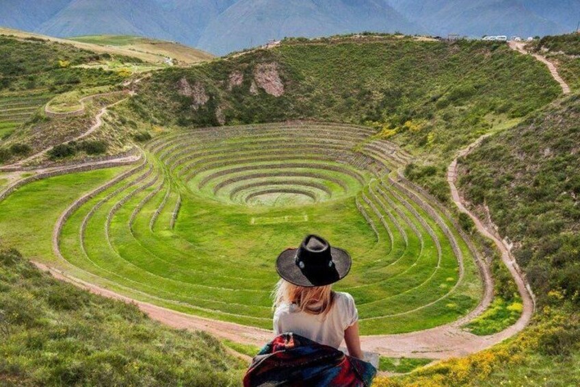 A person in a hat and backpack looking at a large spiral-shaped agricultural field. 3
