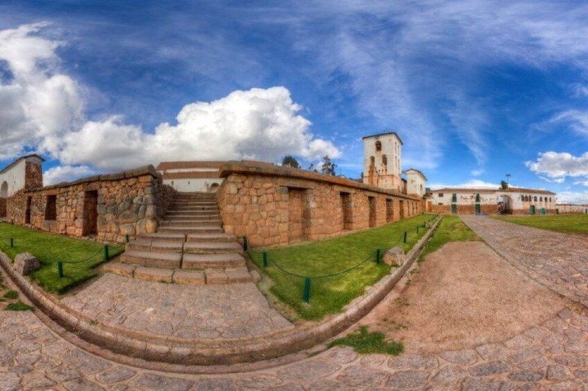 A stone building with a staircase leading up to a tower, surrounded by a grassy area and a paved path. 5