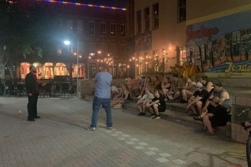 A nighttime outdoor scene with people sitting on steps and a man standing. 4