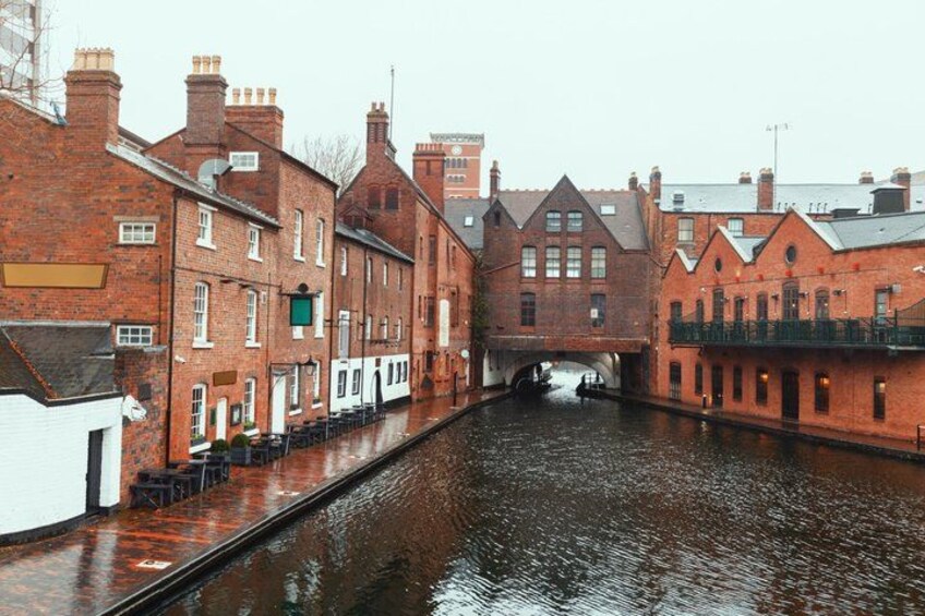 A narrow canal flanked by red brick buildings with a bridge in the distance. 4